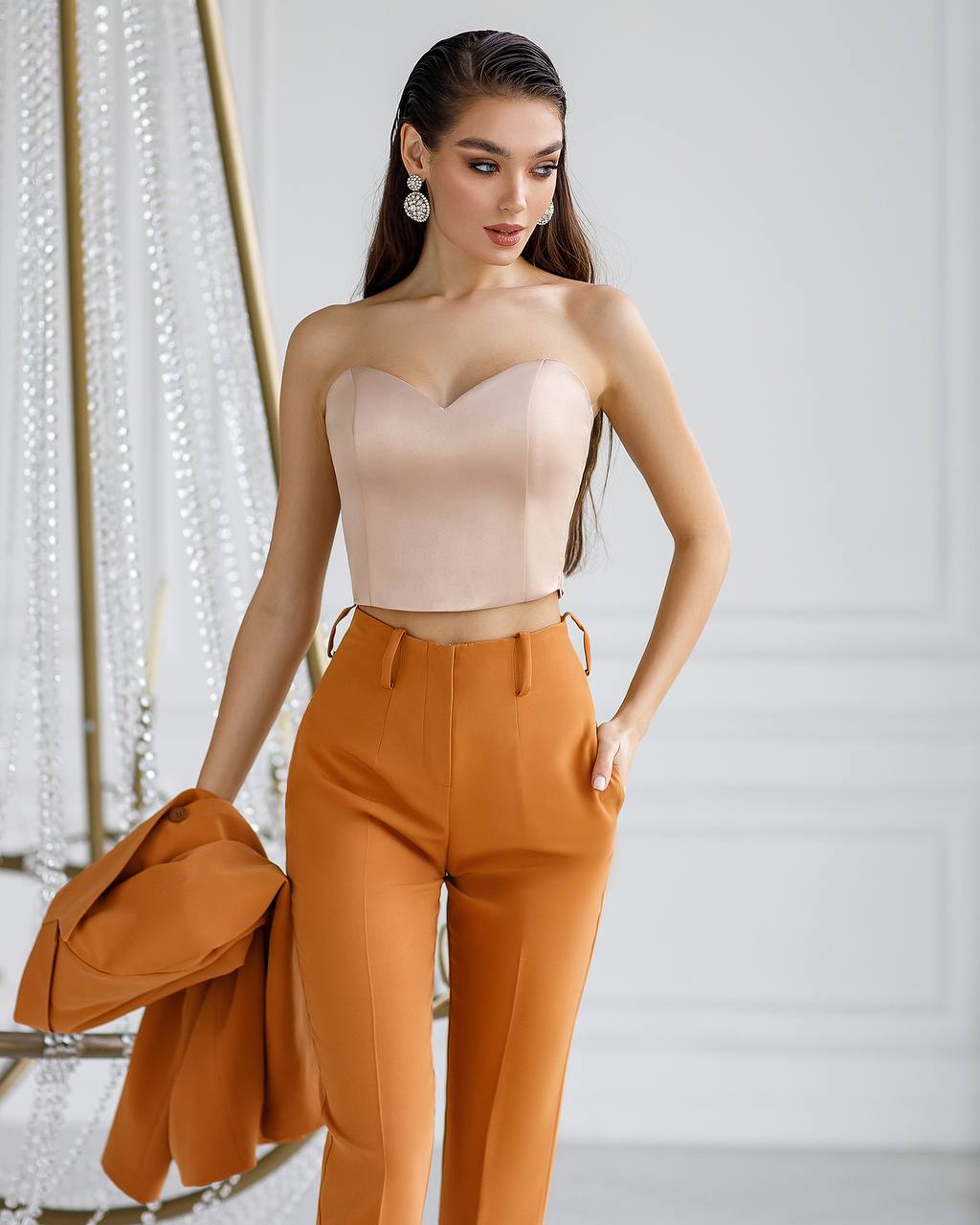 Woman wearing a beige strapless top and orange pants against a white background