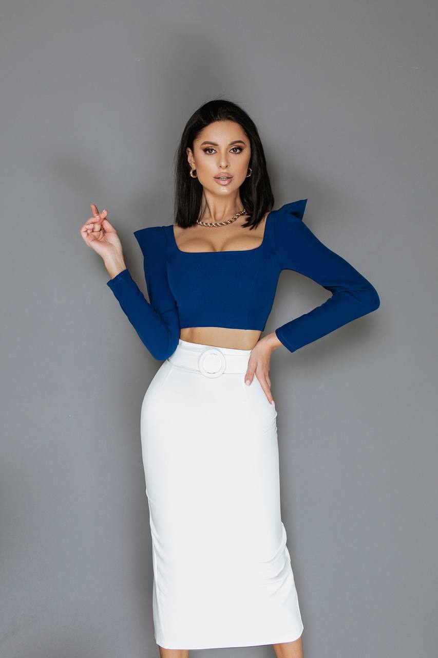 Woman wearing a blue top and white skirt against a gray background