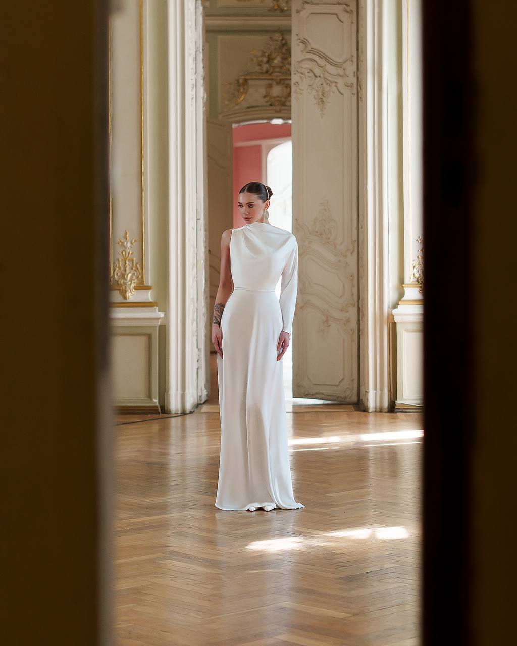 Woman in a white dress standing in an elegant room with high ceilings and decorative walls.