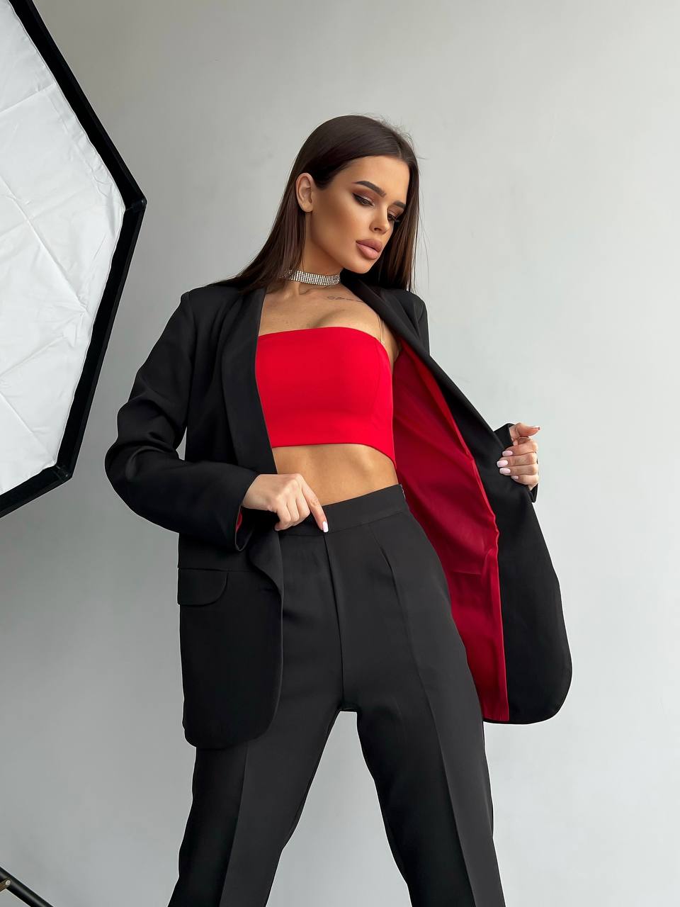 Woman wearing a black blazer over a red top and black pants in a studio setting.