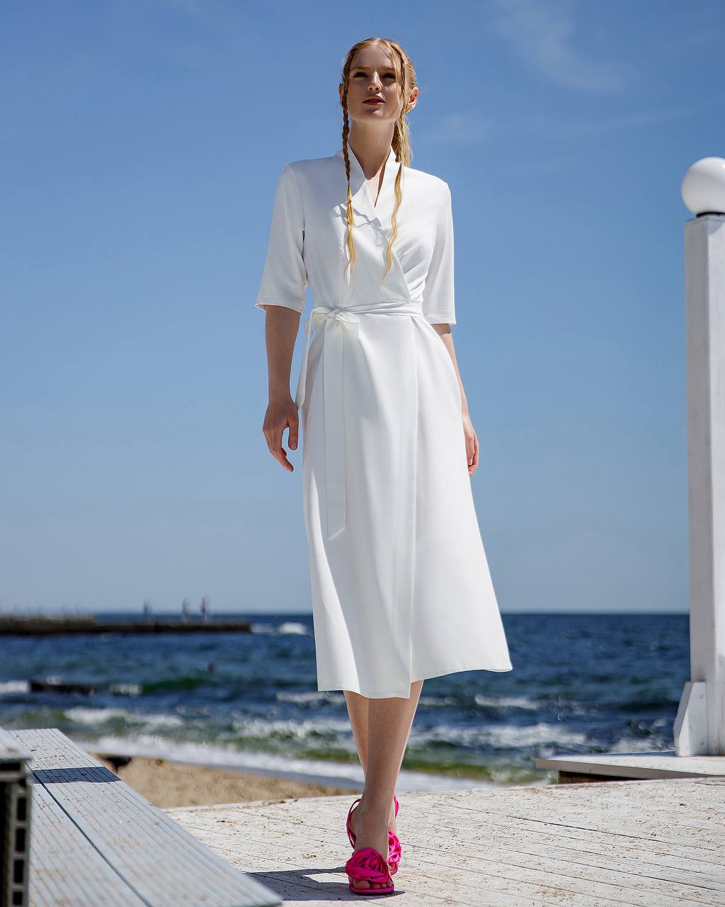Woman in a white dress standing on a wooden platform by the sea
