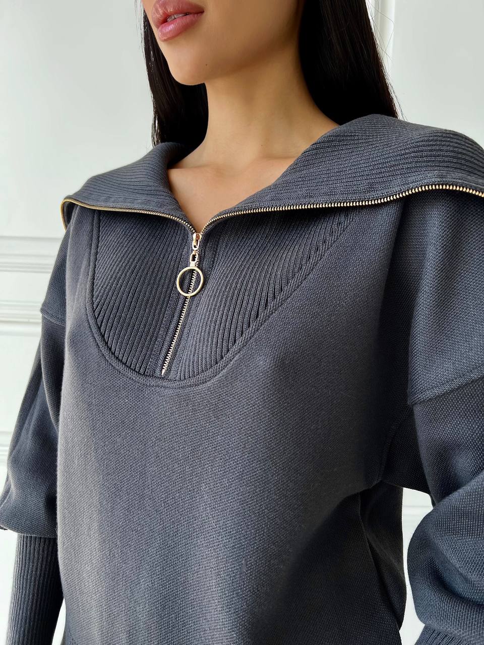 Gray sweater with a zipper detail worn by a person against a white background