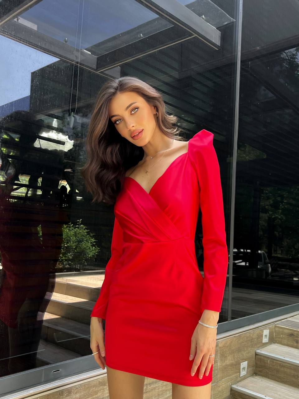 Woman in a red dress standing in front of a reflective glass building.