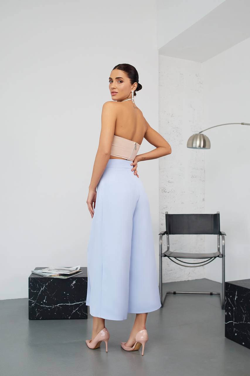 Woman wearing a strapless top and light blue pants in a minimalistic room.