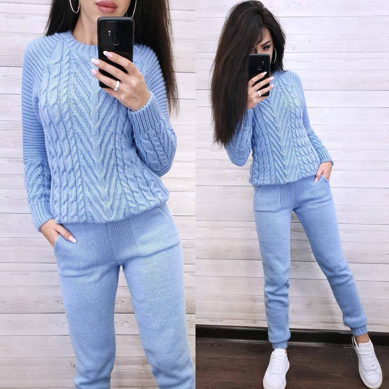 Woman wearing a light blue cable knit sweater and pants, taking a mirror selfie.