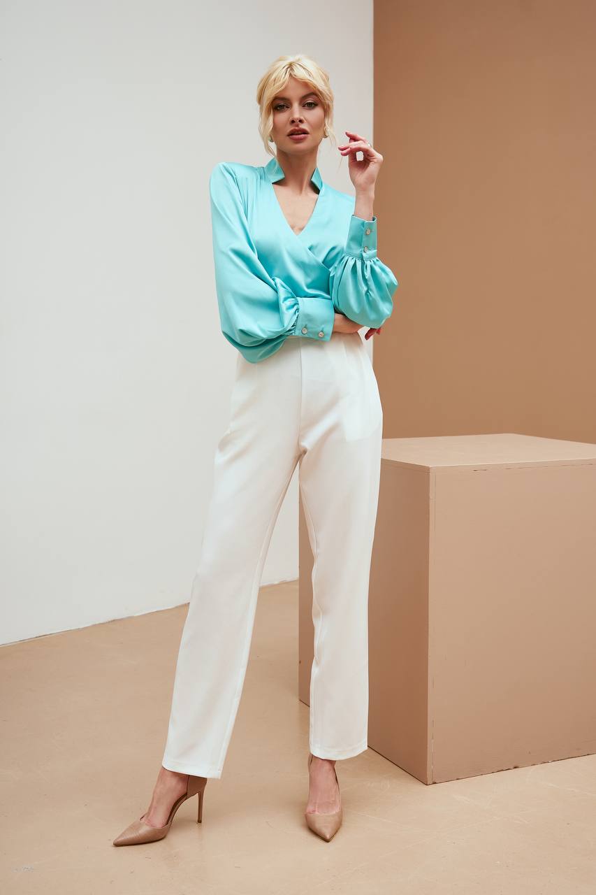 Woman wearing a light blue blouse and white pants against a beige background