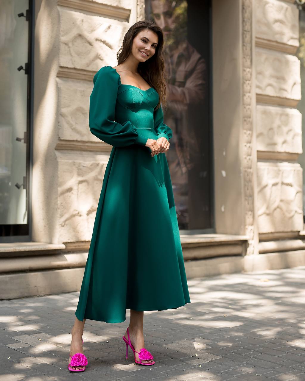 Woman in a green dress with pink shoes standing on a street.