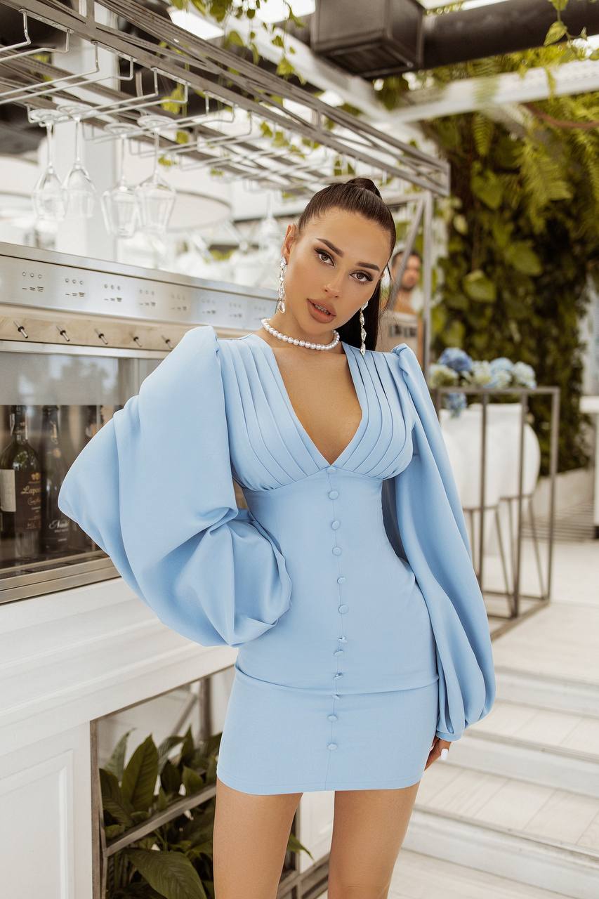 Woman wearing a light blue dress with large sleeves in an indoor setting.