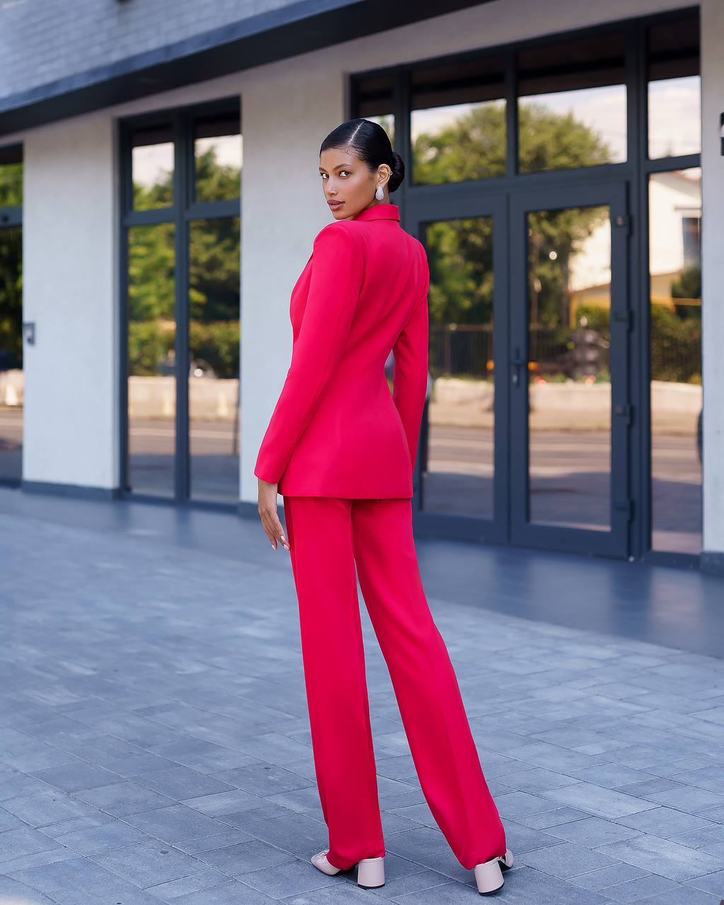 Woman in a bright pink suit standing in front of a modern building.