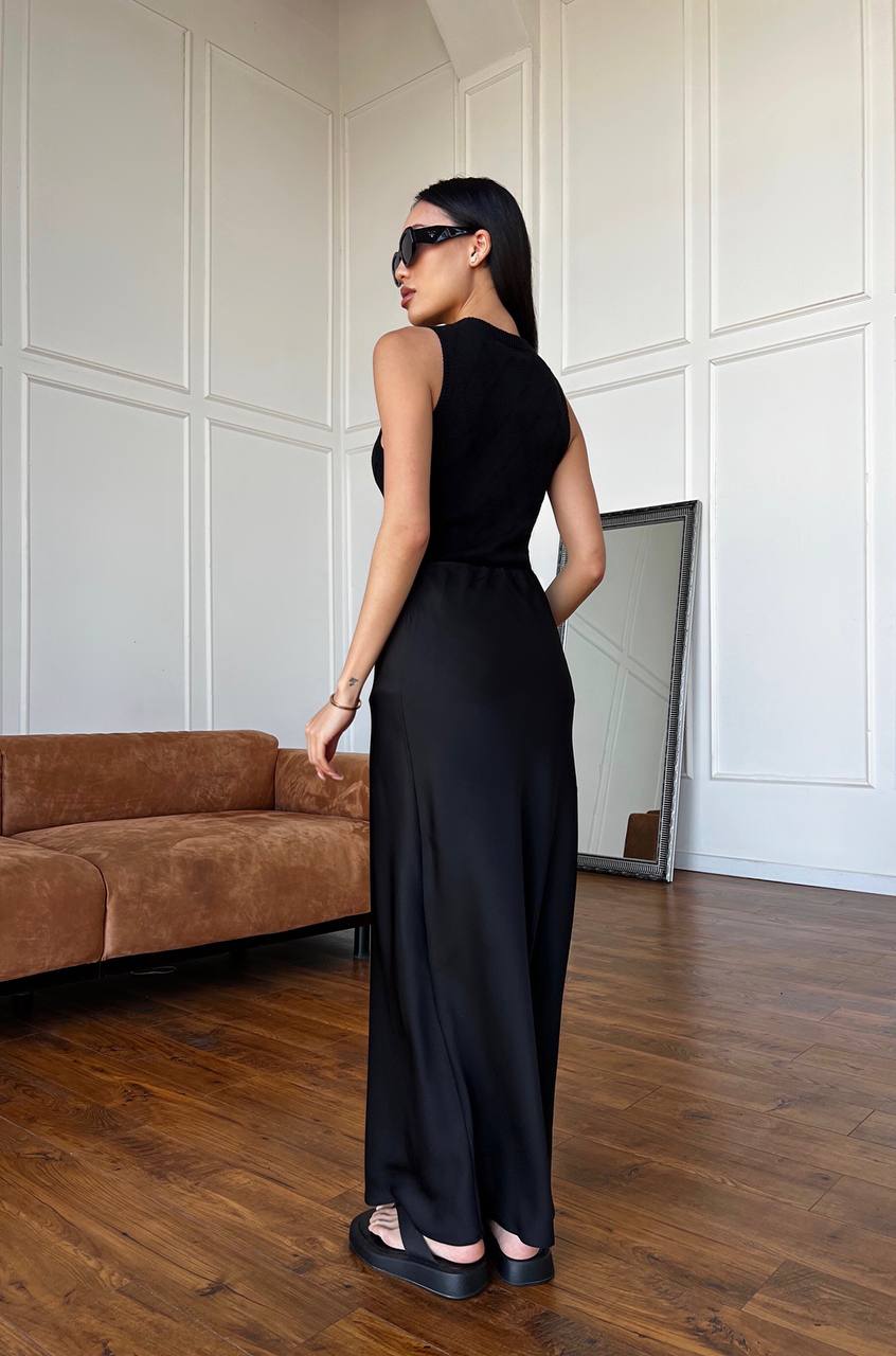 Woman in a black dress standing in a room with wooden flooring and a brown sofa.