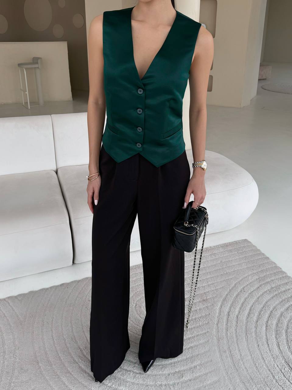 Person wearing a green vest and black pants in a modern living room.