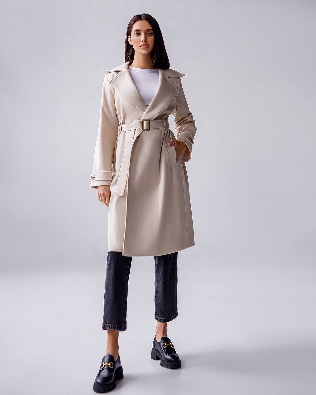 Woman wearing a beige trench coat on a plain background