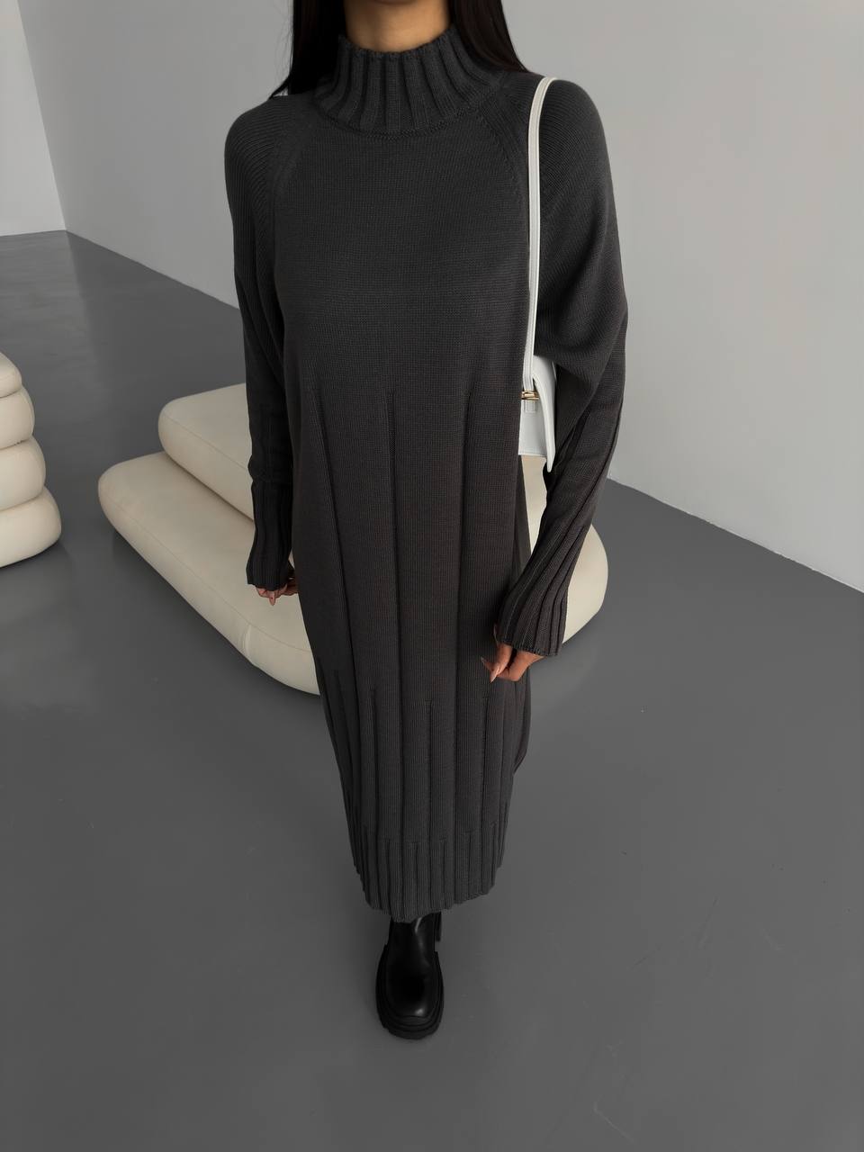 Person wearing a black long-sleeve dress in a minimalistic setting