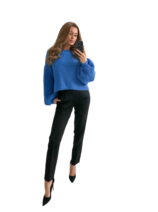 Woman wearing a blue sweater and black pants, standing against a white background