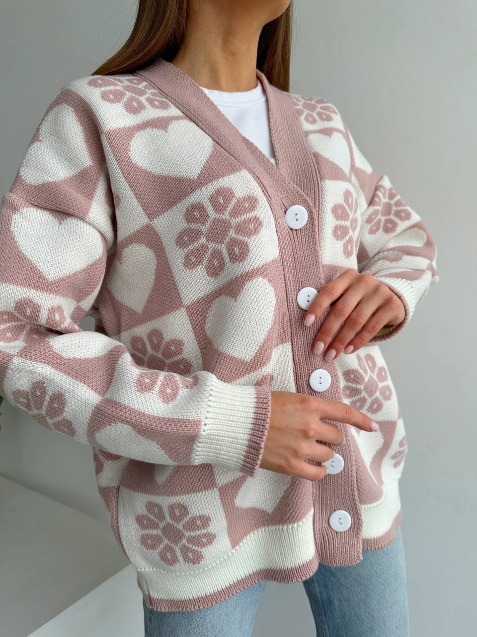 Person wearing a pink and white patterned cardigan with button details on a plain background
