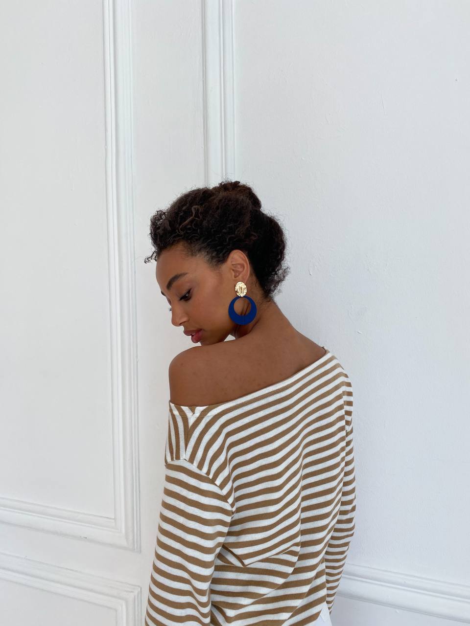 Woman wearing a striped off-shoulder top against a white wall