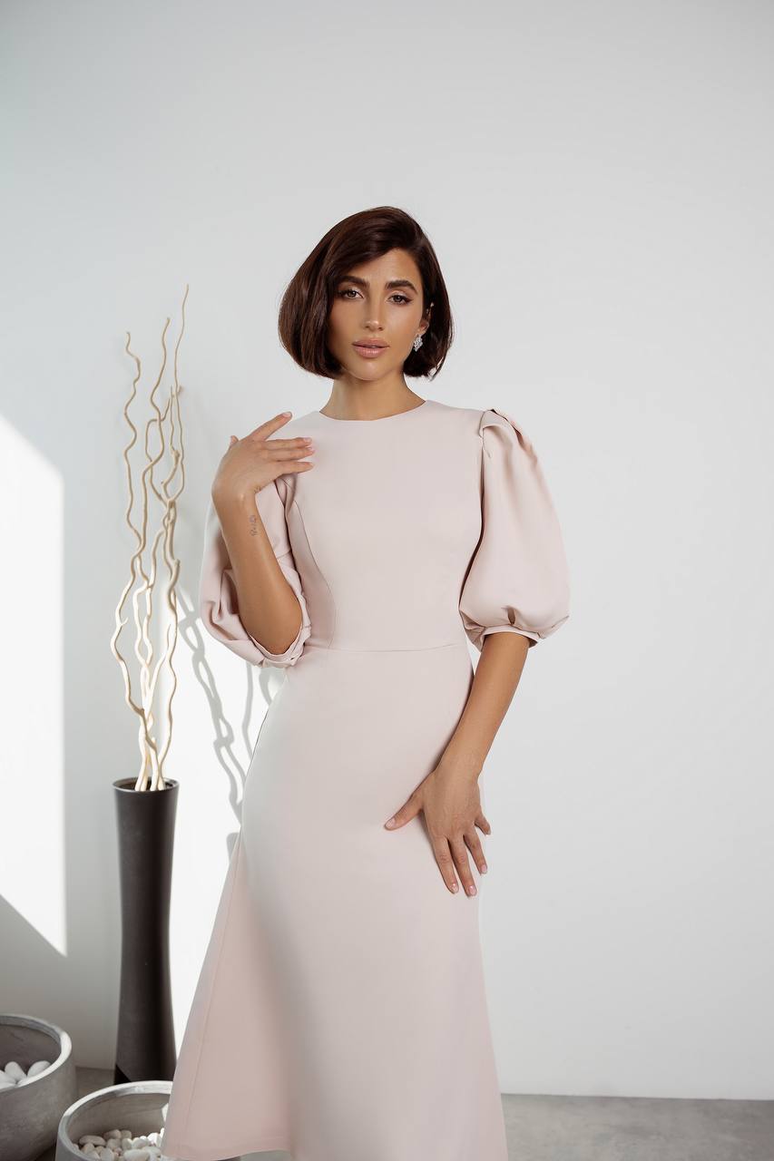 Woman wearing a light pink dress with puffed sleeves in a minimalistic setting.