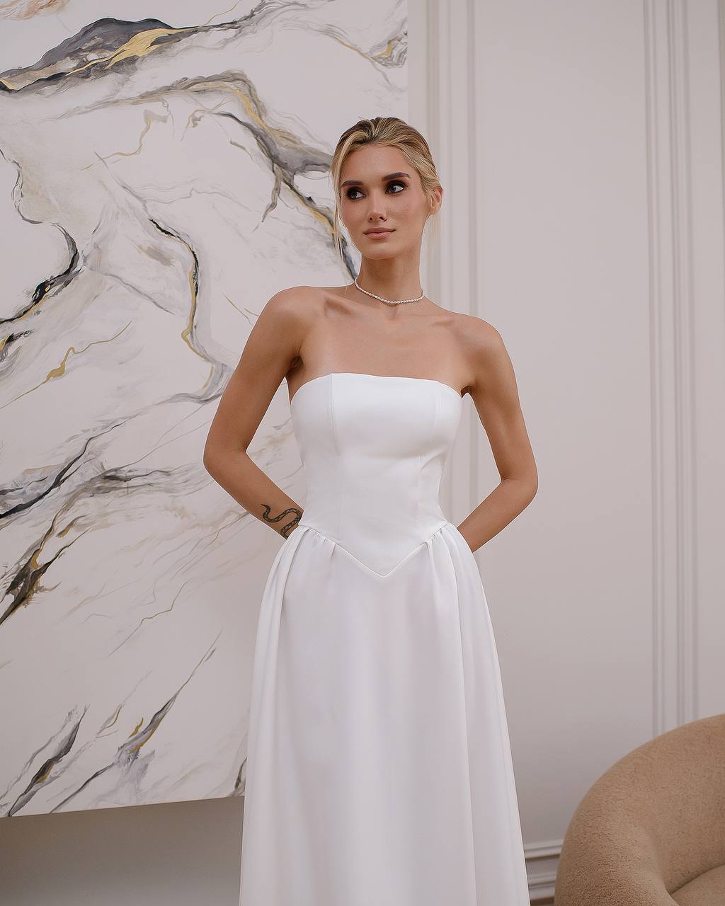 Woman wearing a white strapless dress against a marble wall.