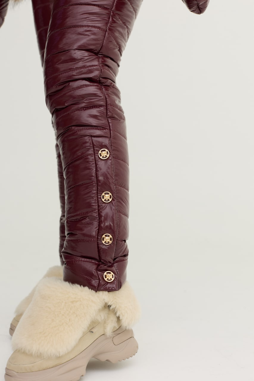 Close-up of maroon quilted pants with gold buttons on a white background