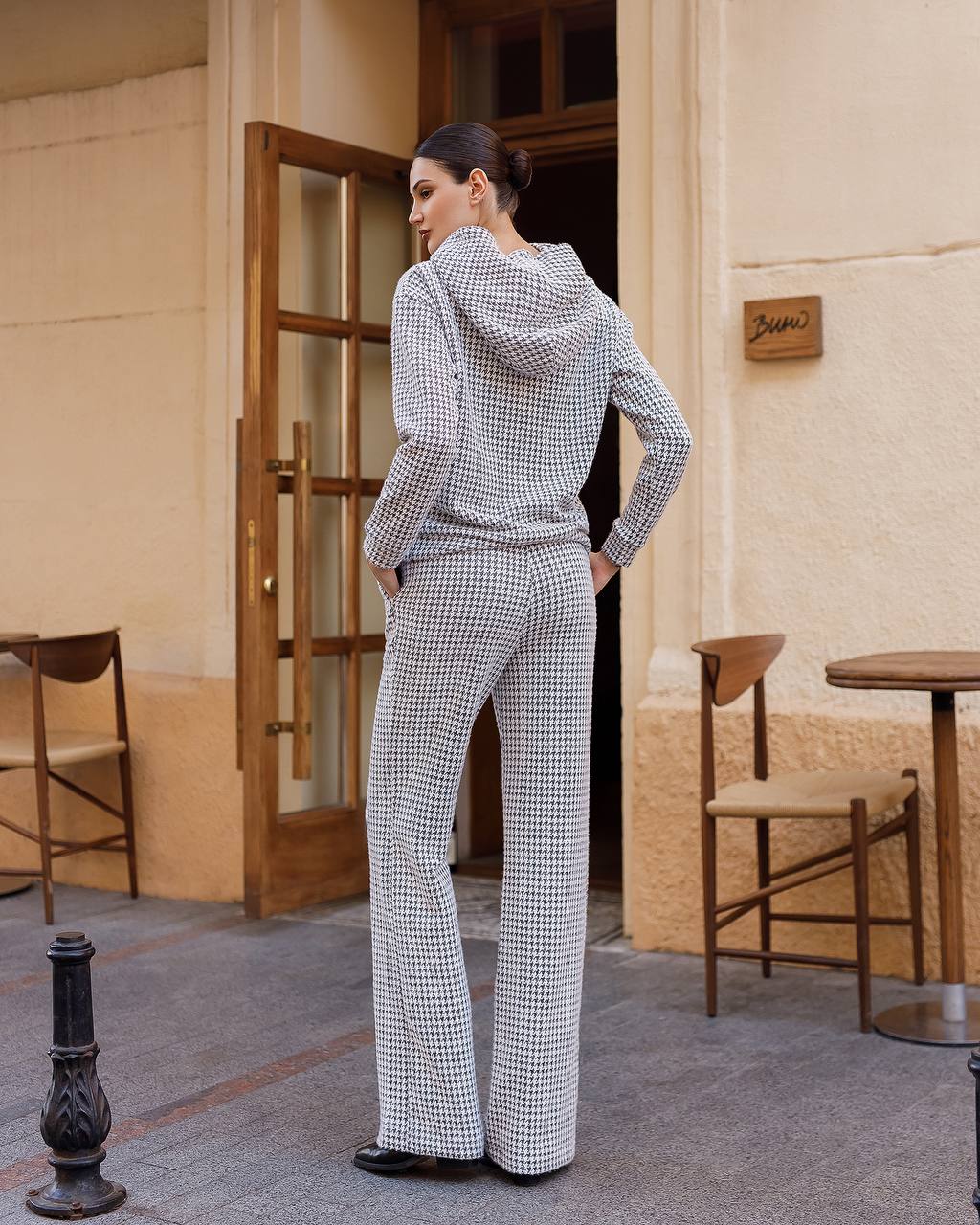 Woman in a checkered outfit standing in an outdoor setting with tables and chairs.