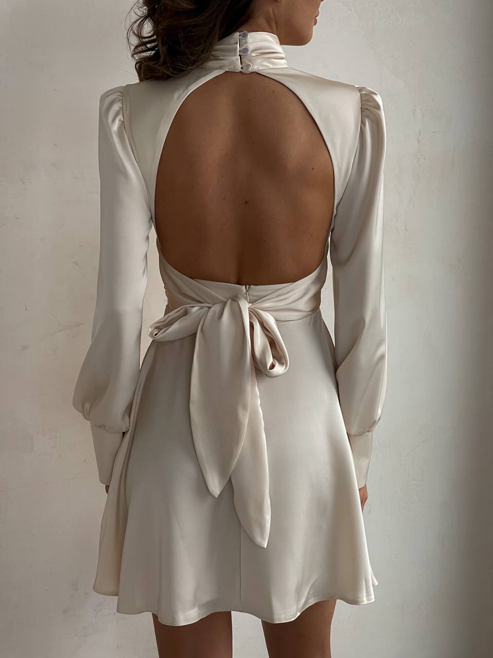 Beige dress with open back and long sleeves on a plain background