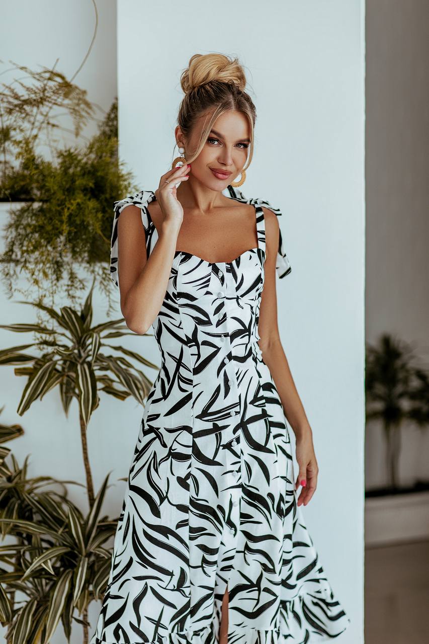 Woman wearing a black and white patterned dress standing indoors with plants in the background