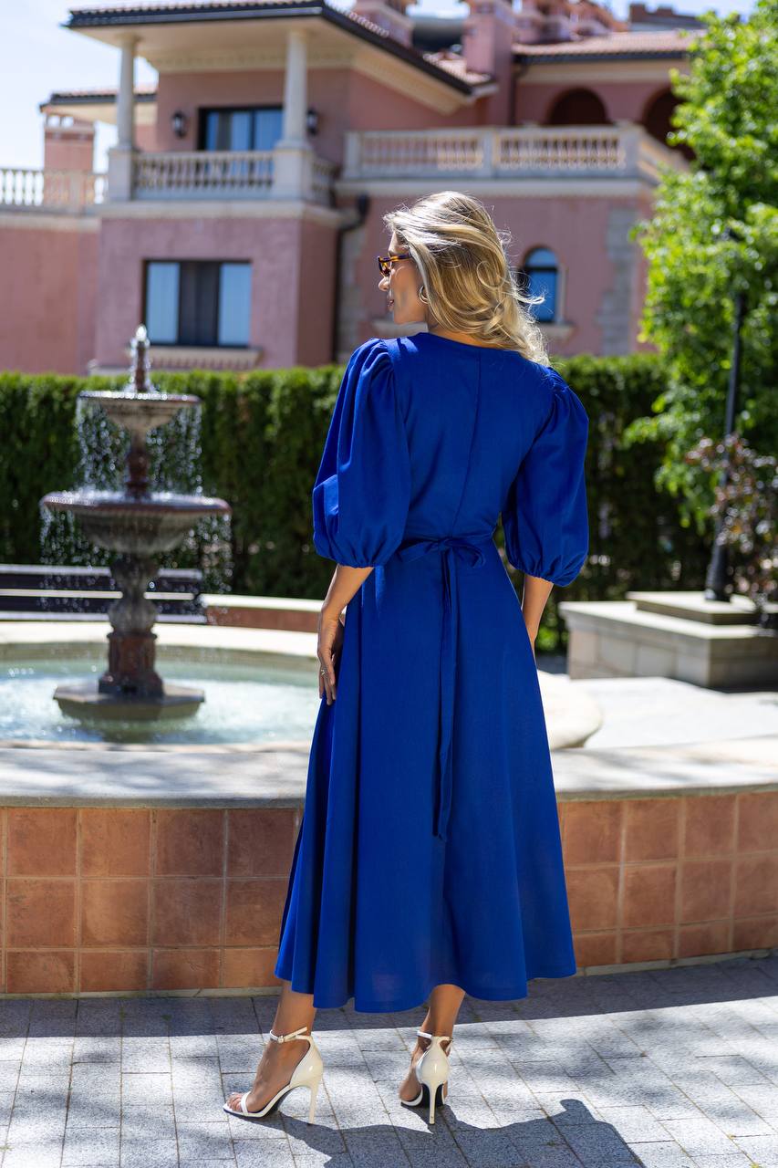 Woman in a blue dress standing in front of a fountain with a building in the background