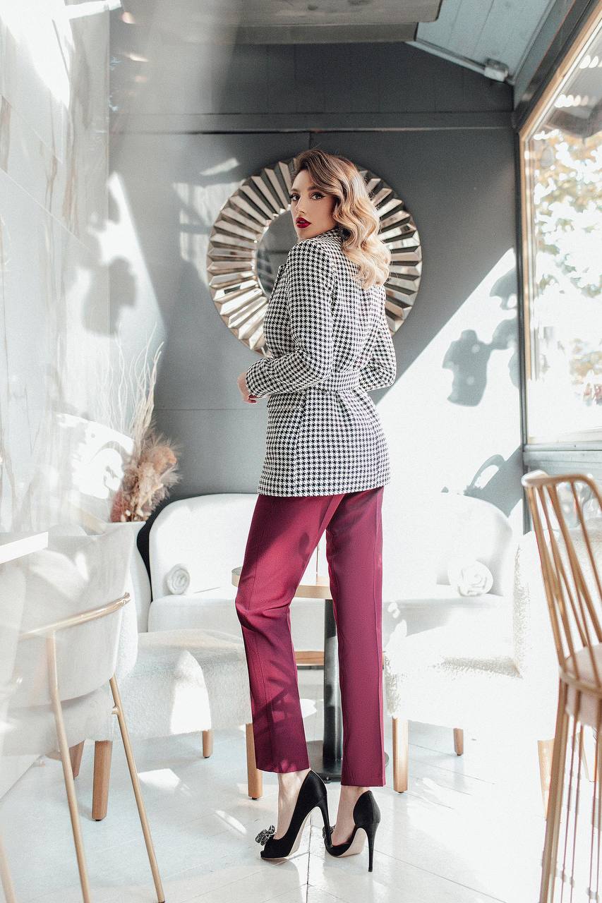 Woman in a stylish outfit with a checkered blazer and red pants standing in a modern interior setting.