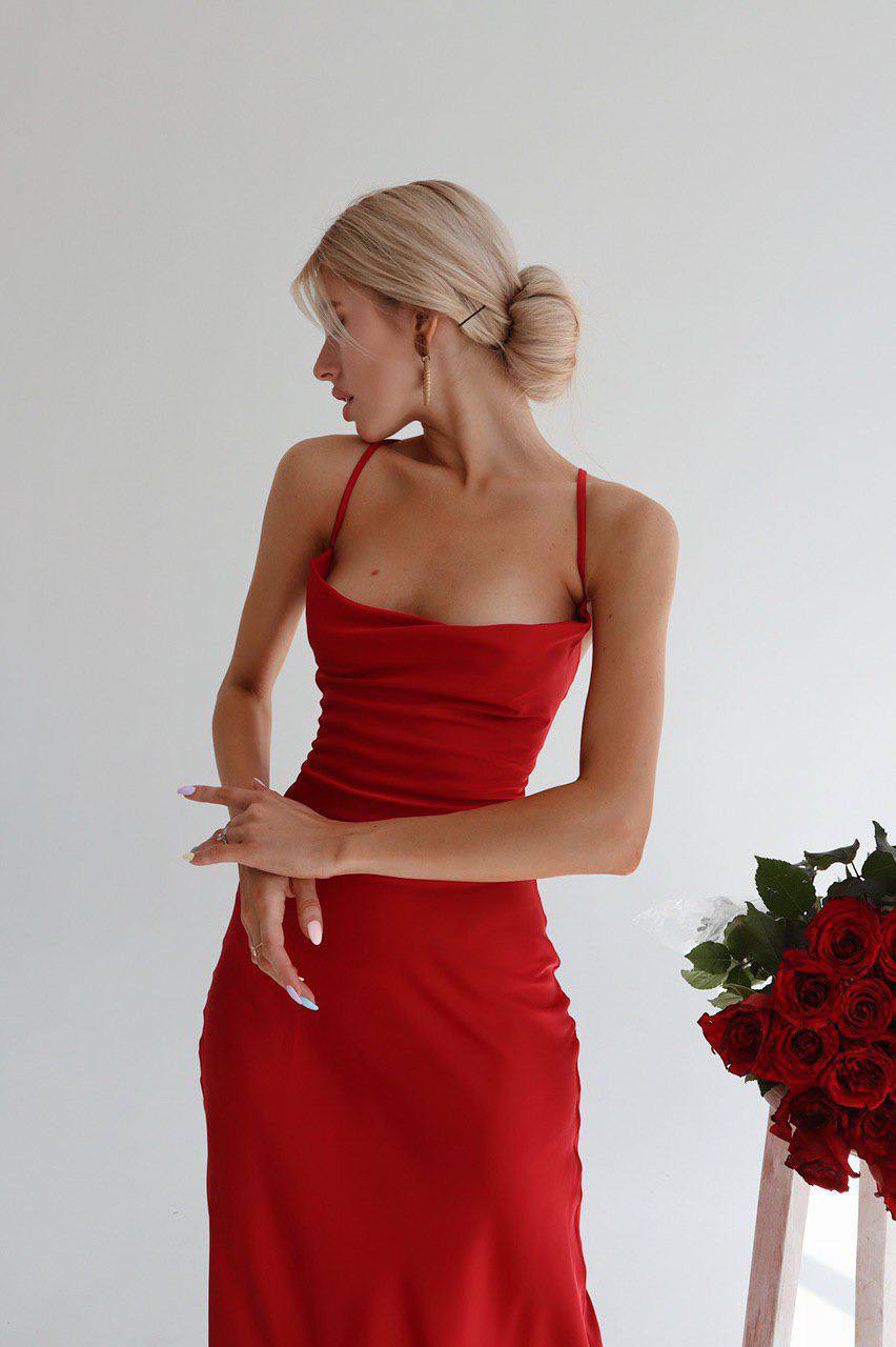 Woman in a red dress standing against a white background with a bouquet of red roses.