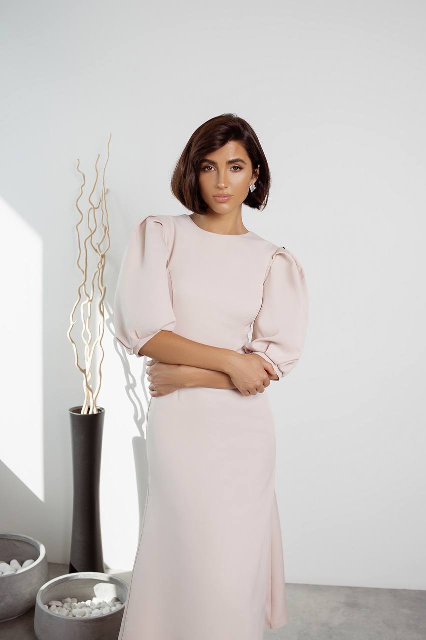 Woman in a light pink dress standing in a minimalistic room with decorative elements.