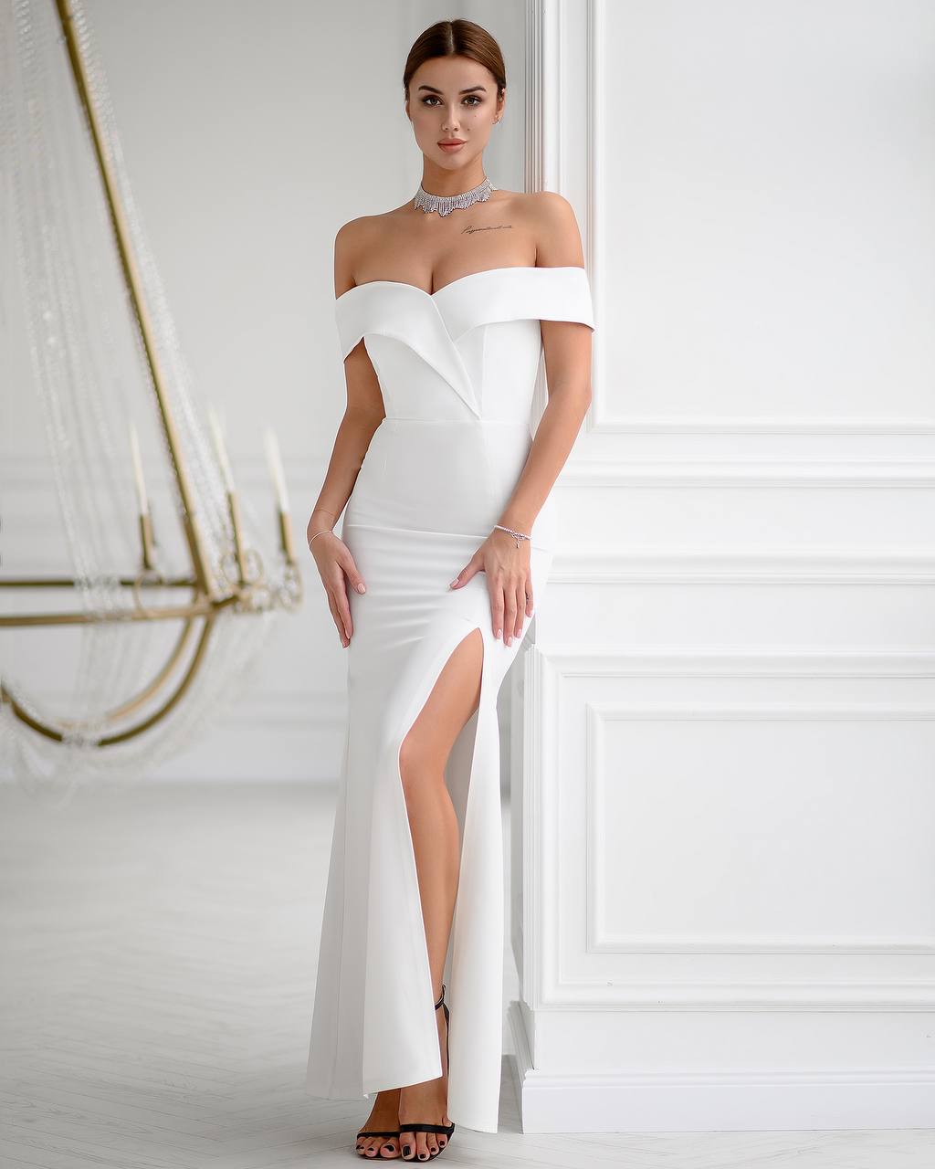 Woman wearing a white off-shoulder gown with a high slit in a elegant interior setting.
