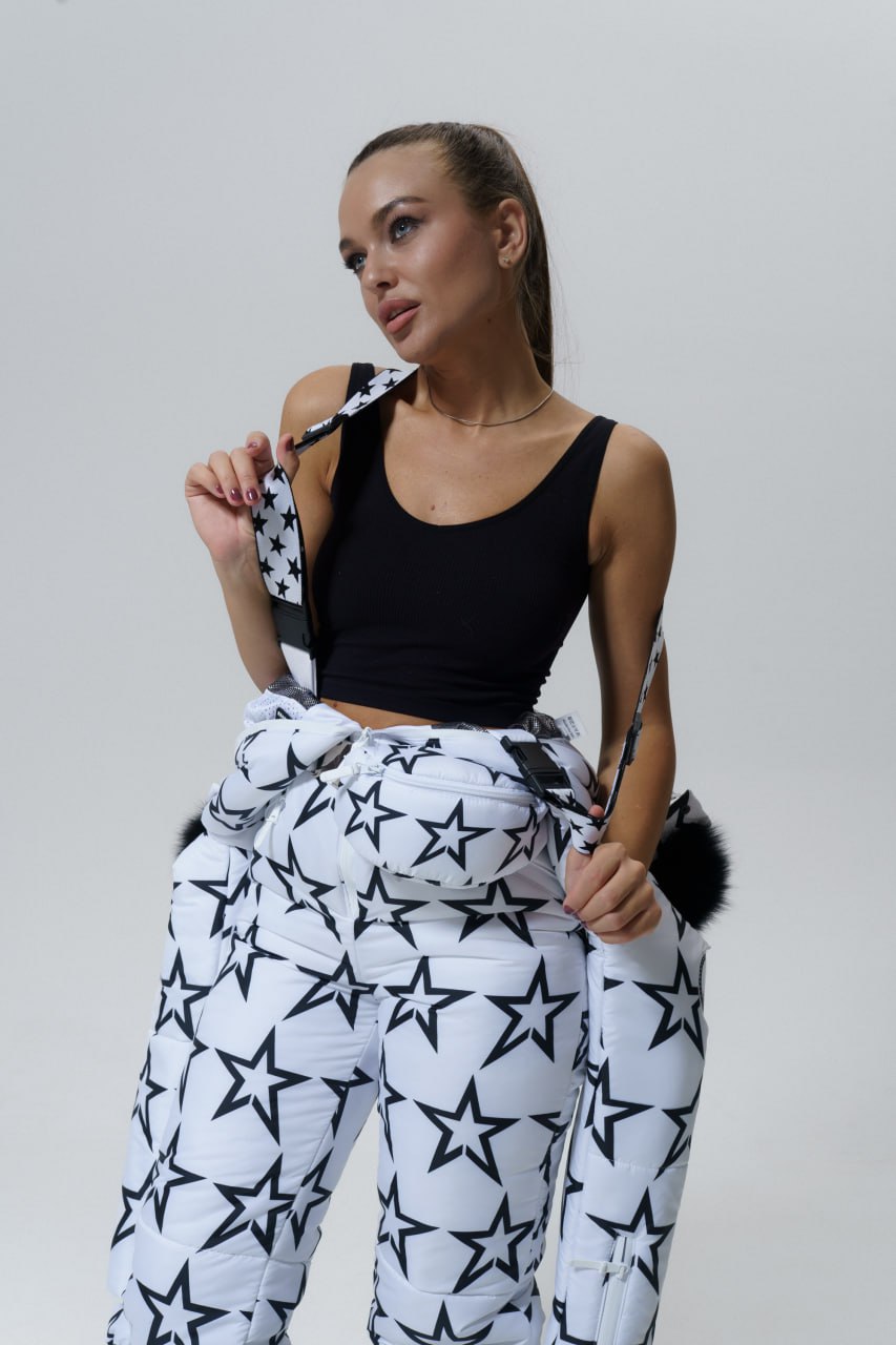 Woman wearing a black top and white pants with star patterns against a plain background