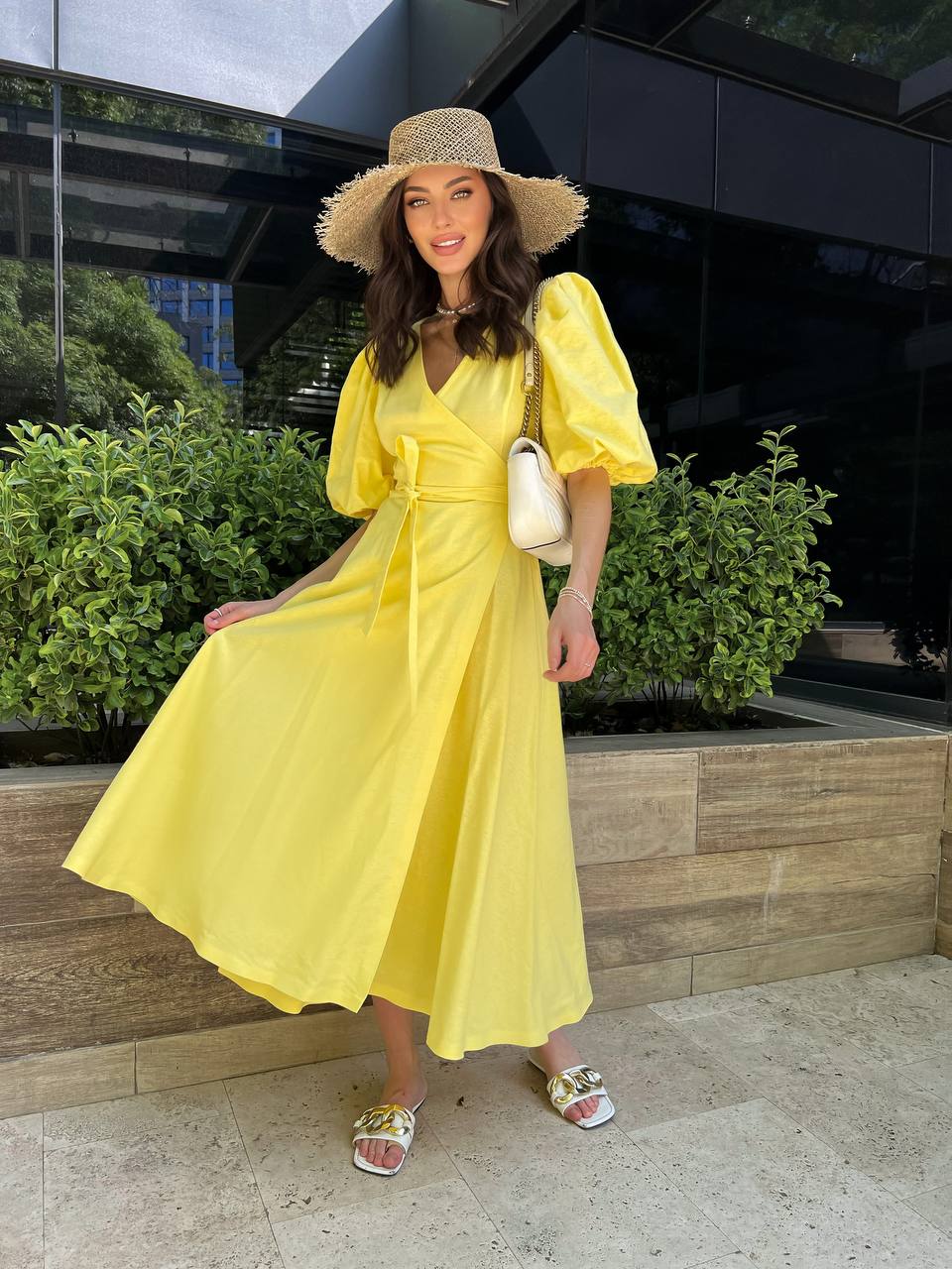 Woman in a yellow dress and straw hat standing outdoors.