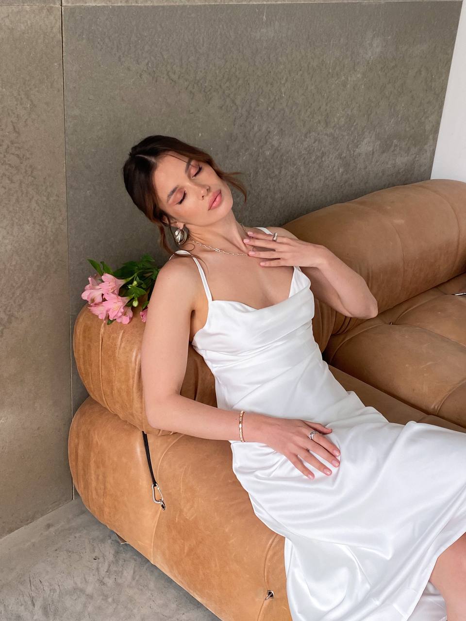 Woman in a white dress sitting on a brown sofa with a neutral wall background
