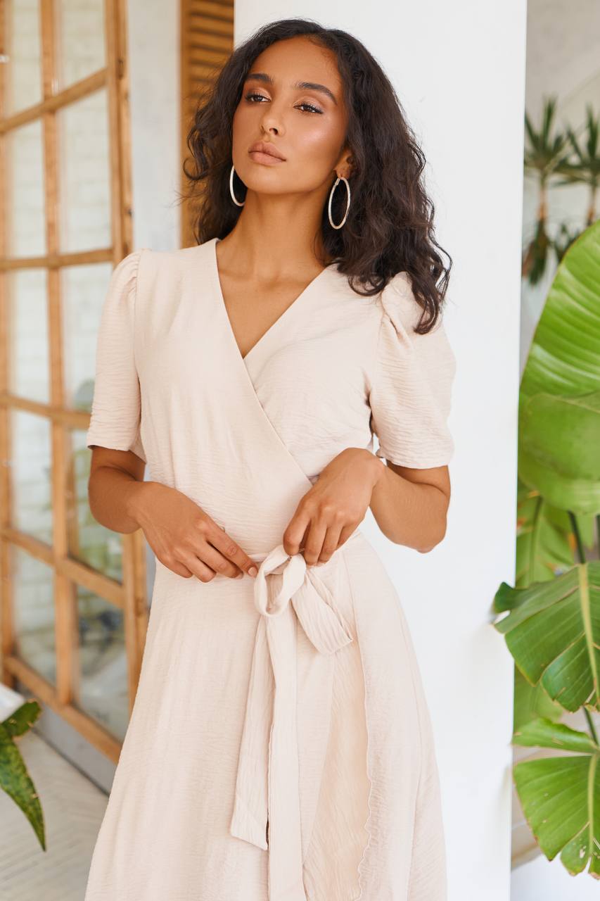 Woman wearing a beige wrap dress with a blurred indoor background