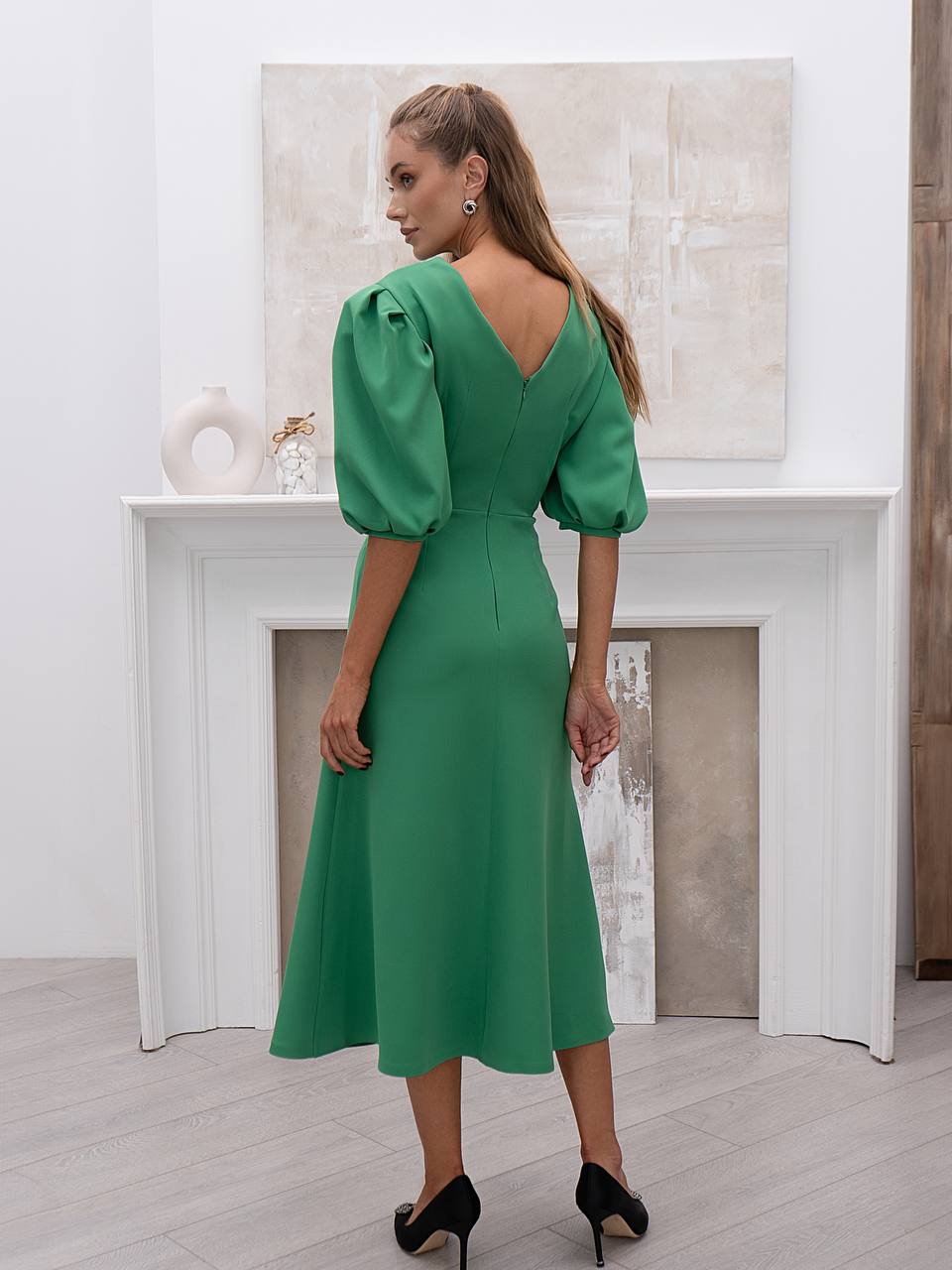 Woman wearing a green dress with puff sleeves in a minimalistic room.