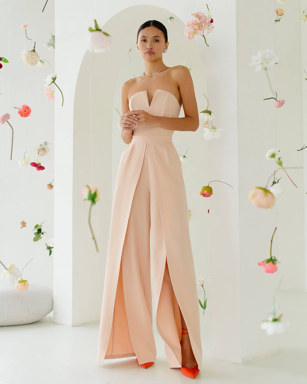 Woman wearing a strapless blush pink gown with a slit in a floral decorated room.