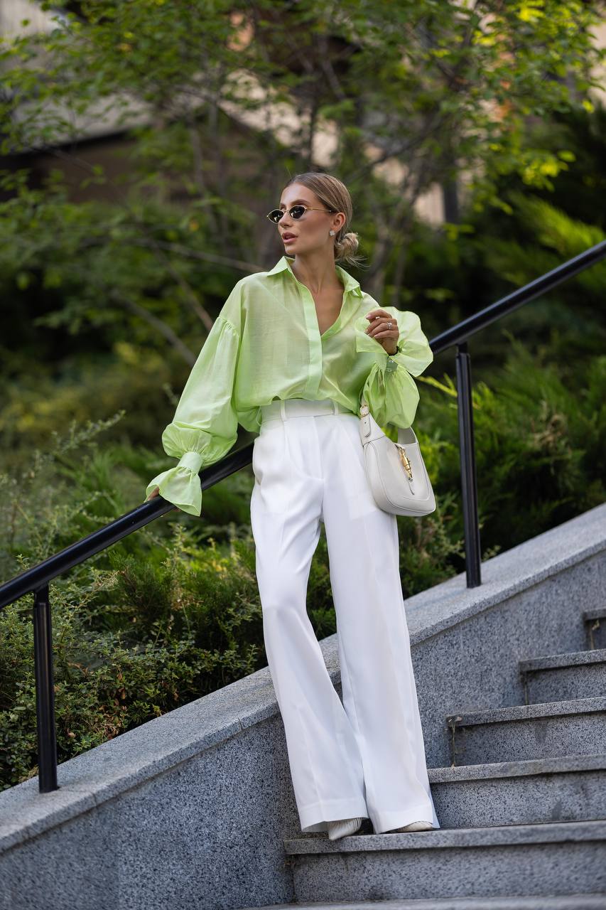 Woman in a green shirt and white pants standing on steps with greenery in the background