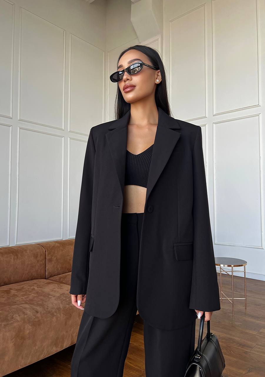 Woman in a black outfit standing in a room with a neutral wall and brown couch.