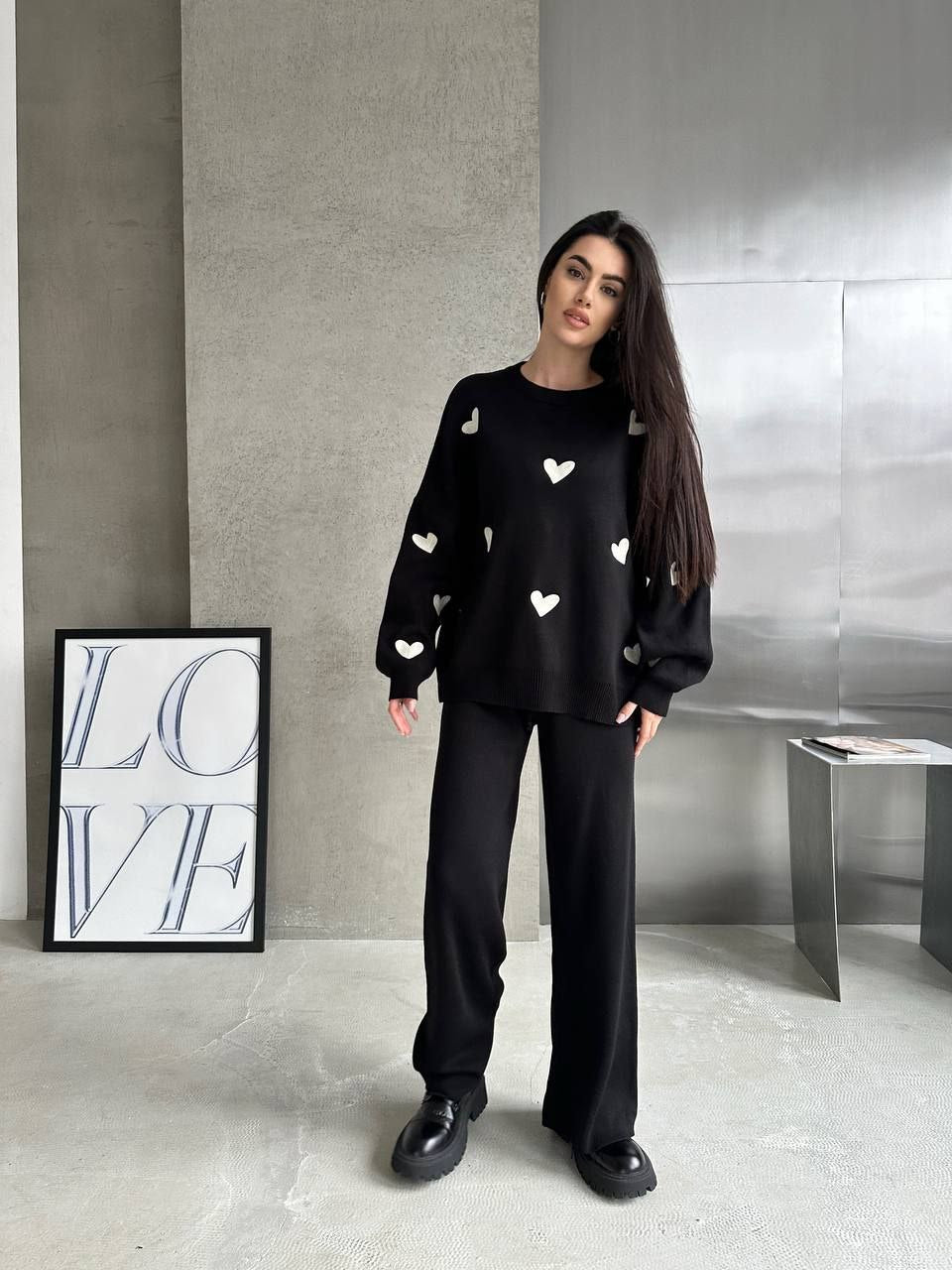 Woman wearing a black sweater with white heart patterns in a modern interior setting.