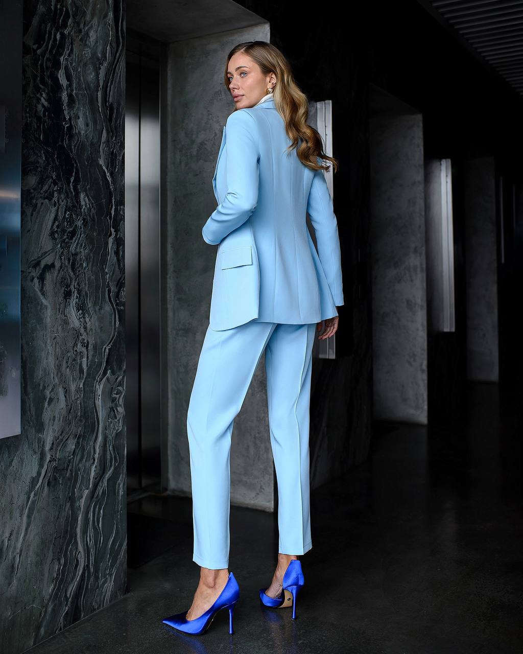 Woman in a light blue suit standing in a modern interior setting.