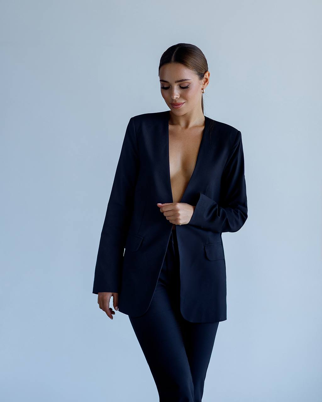 Woman wearing a black suit with a plunging neckline against a light gray background