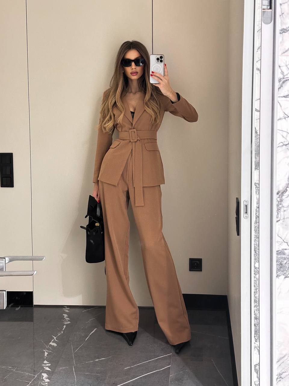 Woman taking a mirror selfie wearing a beige suit in an indoor setting.