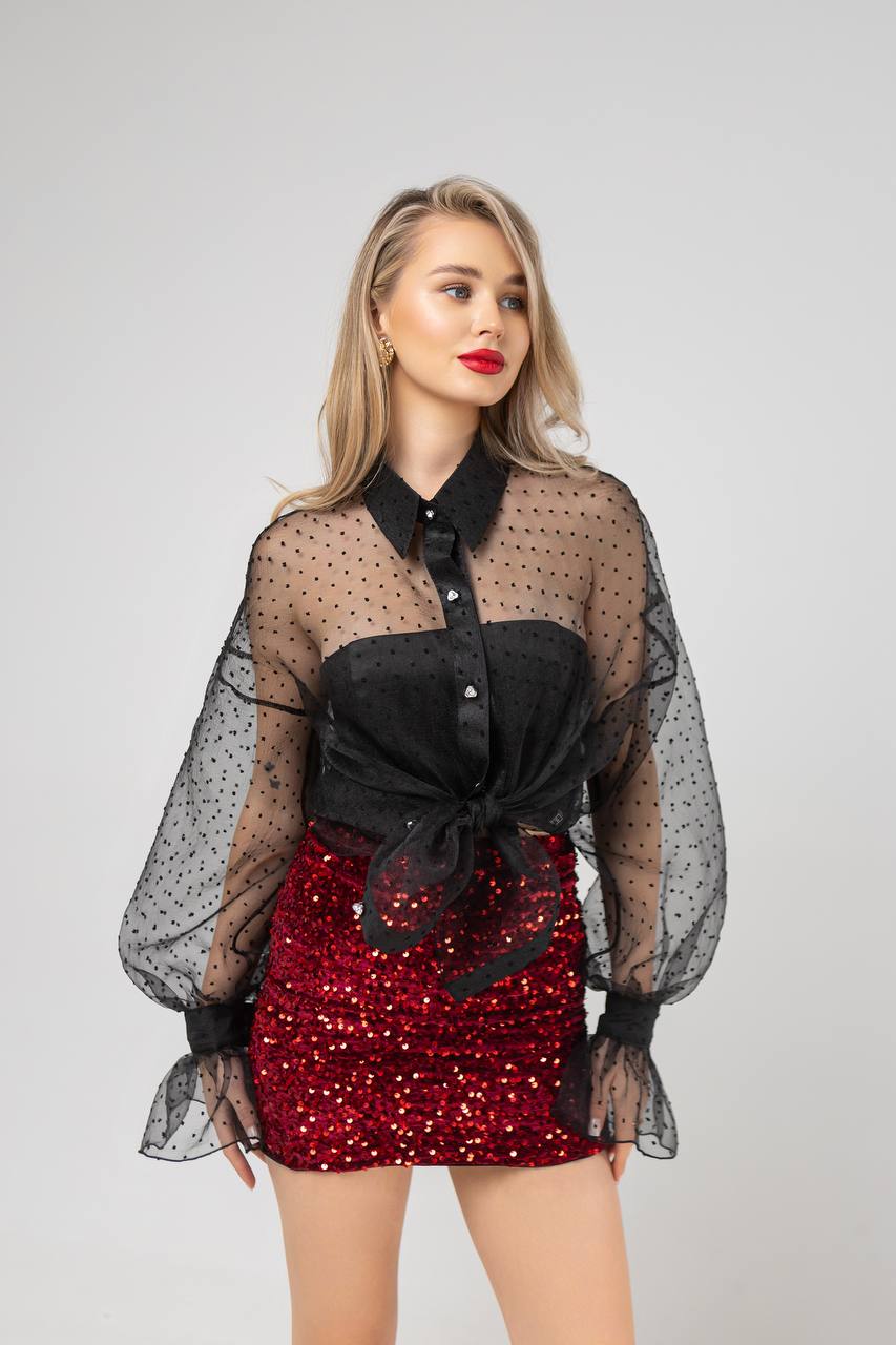 Woman wearing a black sheer top with a red sequin skirt on a gray background