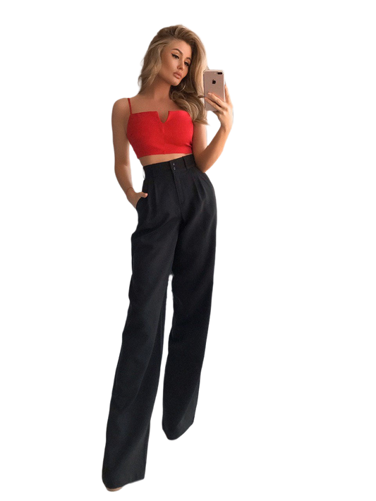 Woman taking a selfie wearing a red top and black high-waisted pants on a white background