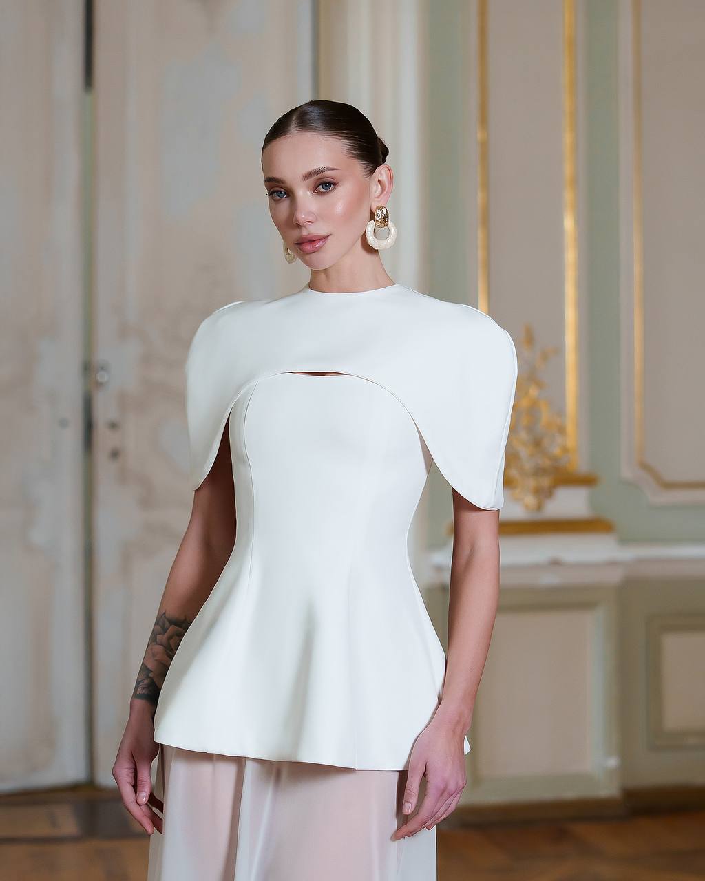 Woman wearing a white outfit with a unique design in an elegant interior setting