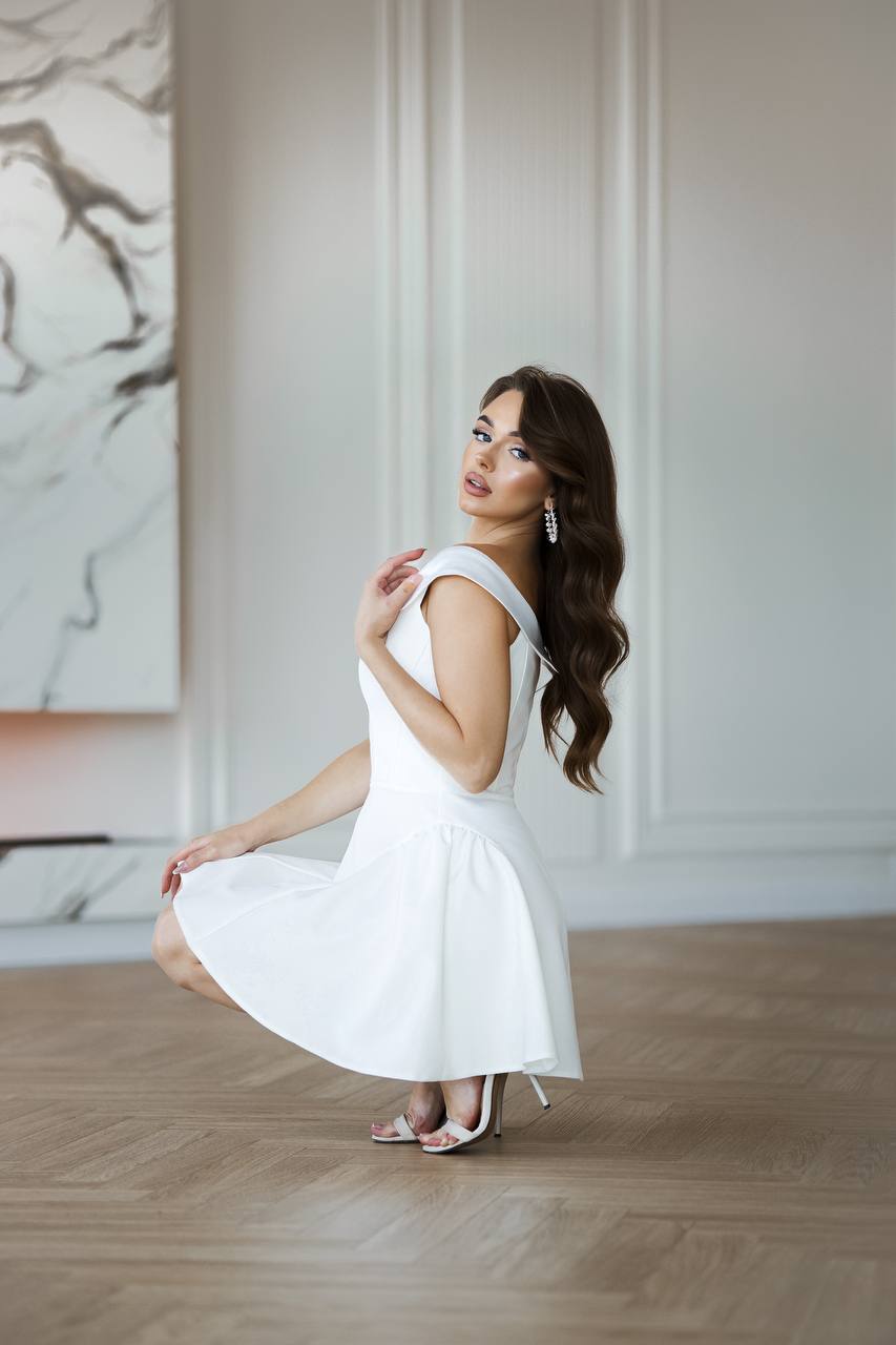 Woman in a white dress posing in a room with marble wall art.