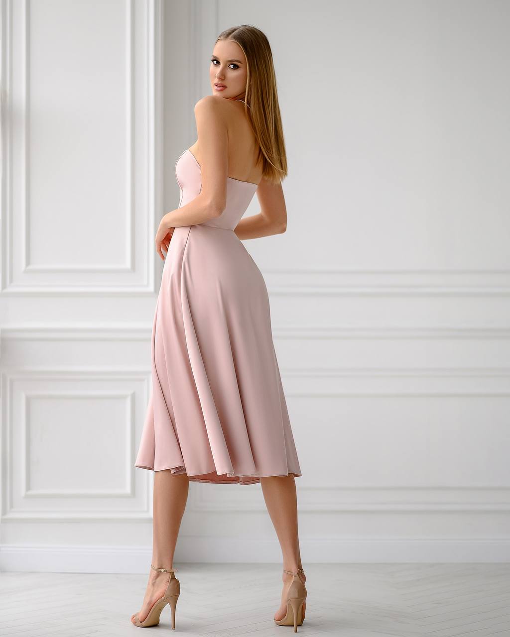 Woman wearing a pink strapless dress against a white wall