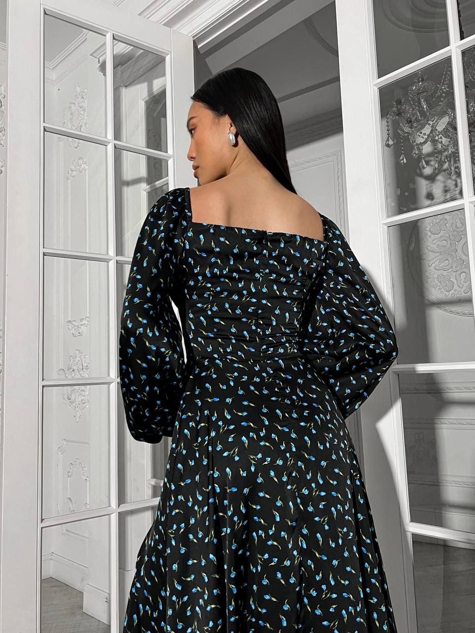 Woman wearing a black dress with blue patterns in a room with white walls and a window.