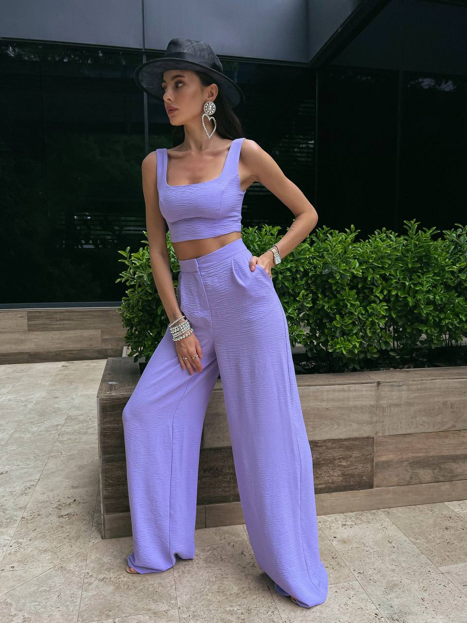Woman in a lavender outfit standing outdoors with greenery in the background